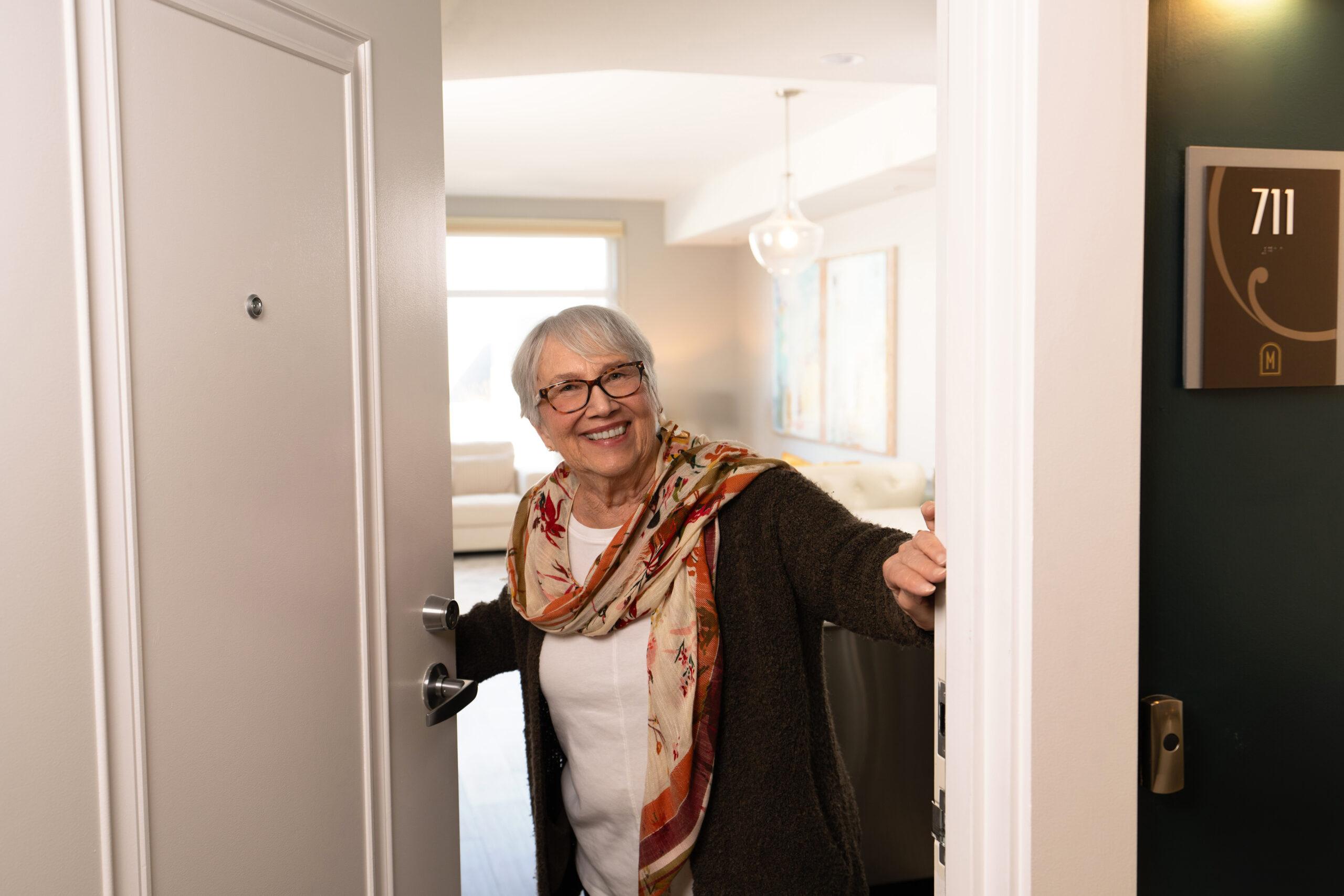 A photo of a cheerful woman opening the door to her apartment.