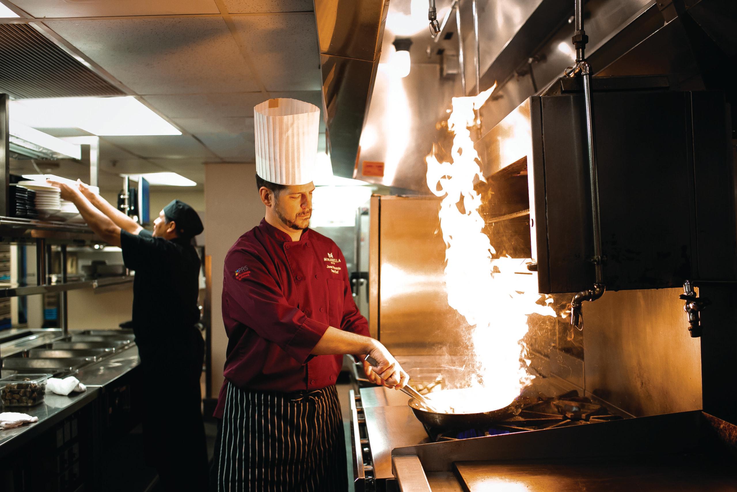 Cinematic photo of a chef flipping a wok, whose contents are on fire.
